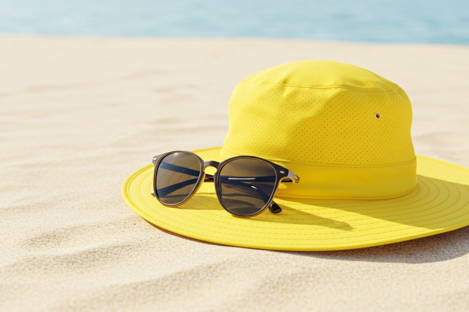 A vibrant yellow sun hat and stylish sunglasses resting on the warm golden sand of a beautiful tropical beach during a perfect summer holiday